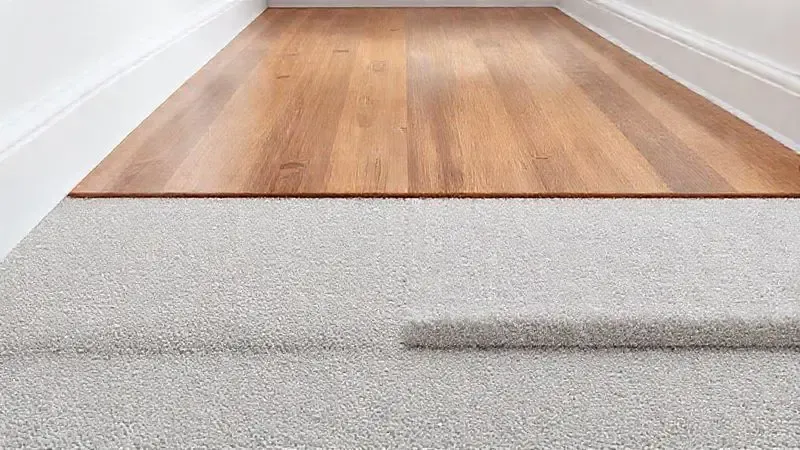 Render 3D de uma superfície dividida ao meio, mostrando piso laminado de madeira de um lado e um tapete de outro, para ilustrar o desempenho em diferentes pisos.
